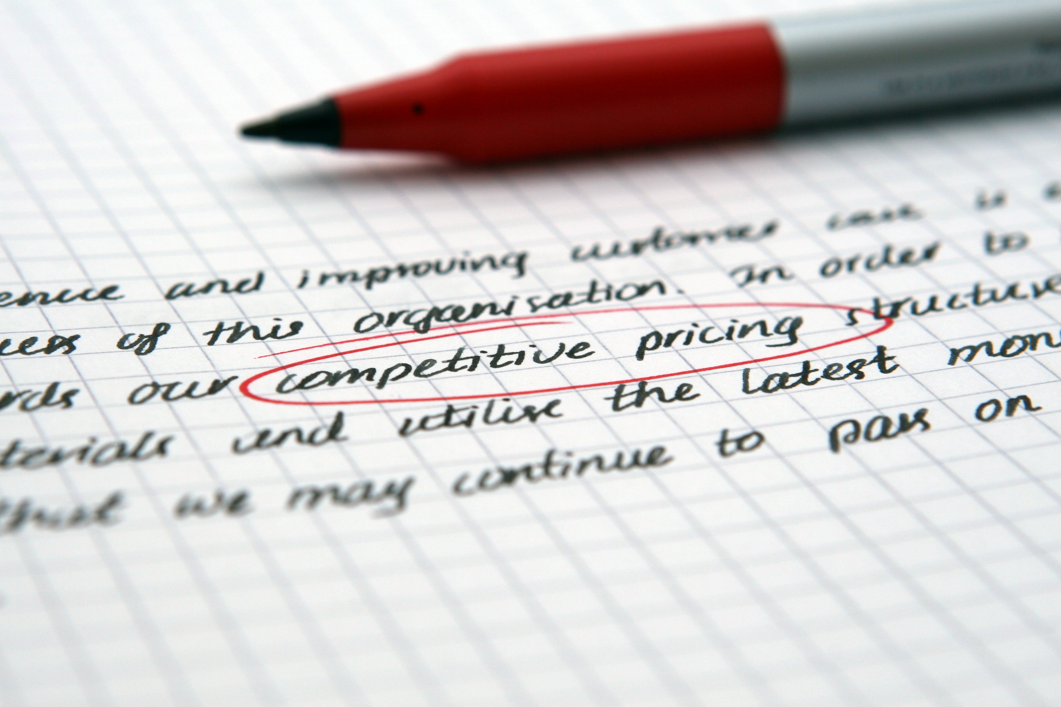 								 Red pen laying on a sheet of paper with words competitive pricing circled in red. 								 				